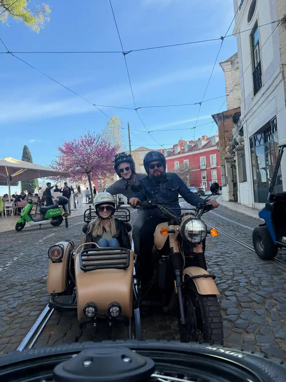 A couple in a tan sidecar on a cobbled street under blossom