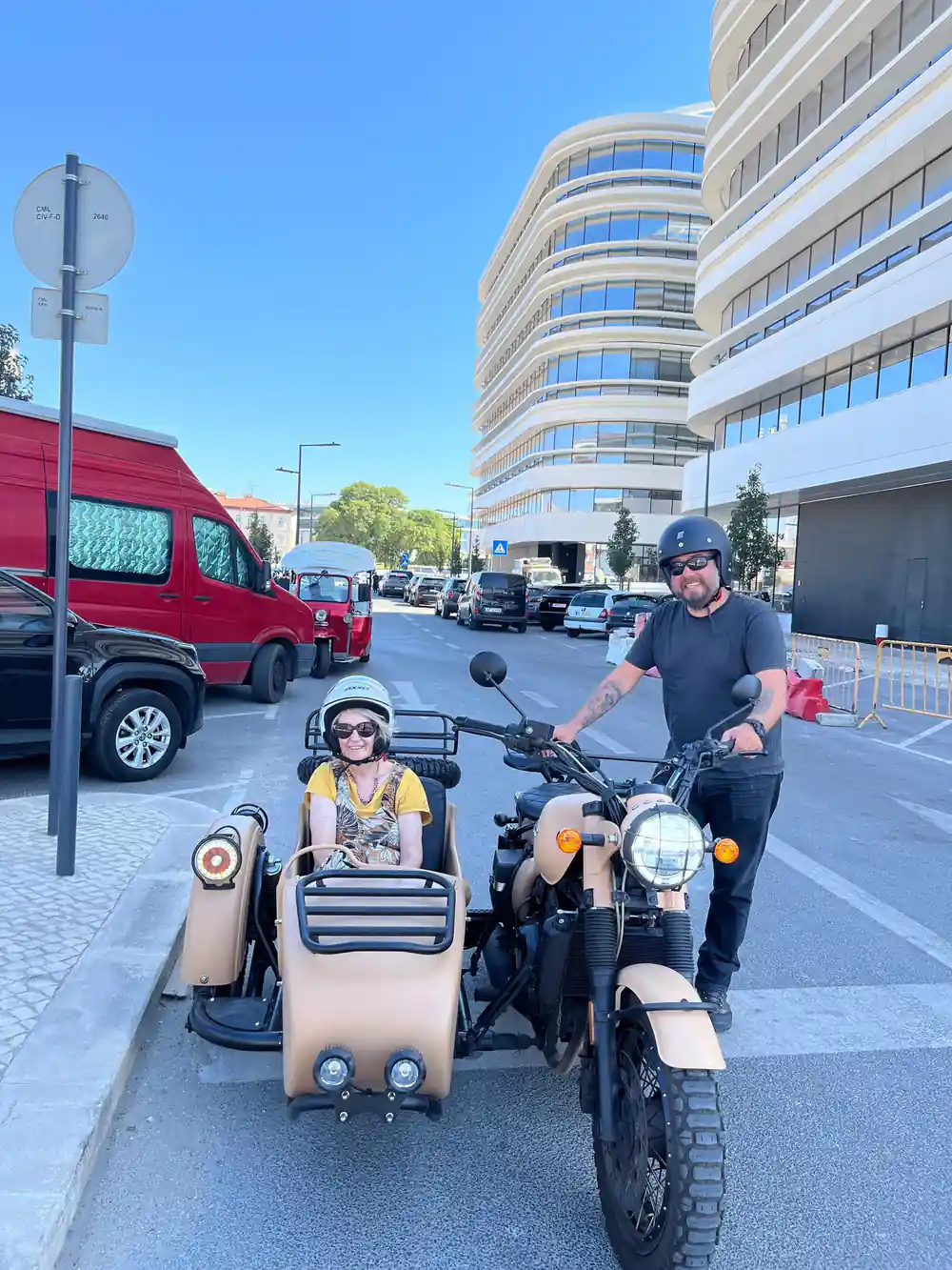 A driver standing by a tan sidecar with a passenger in the chair