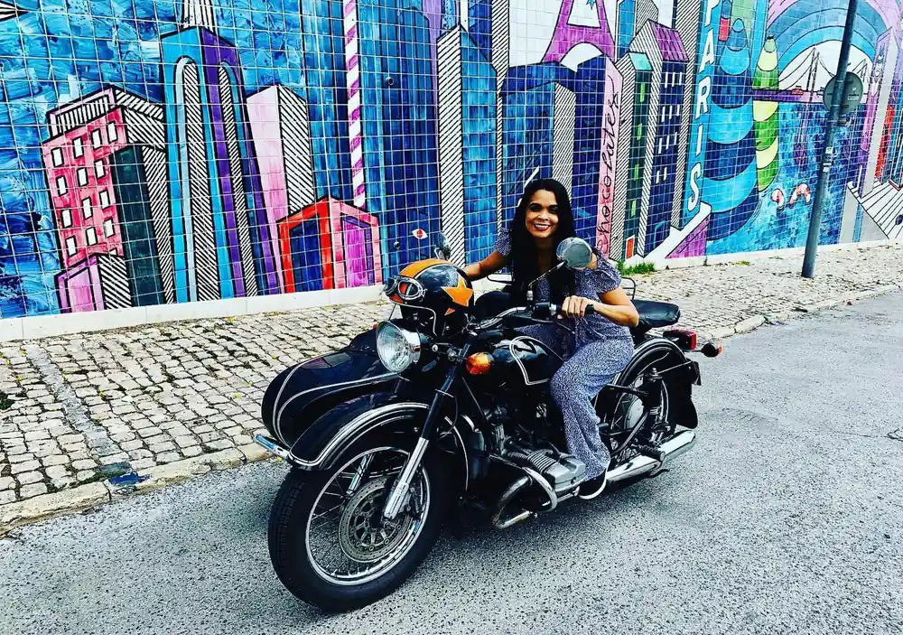 A rider in a sidecar in front of a wall painted in bright mural colours