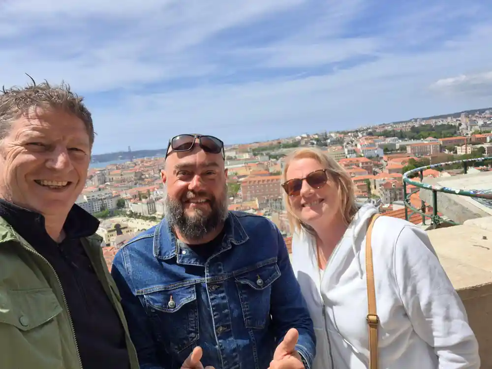 Three people at a railing above a wide spread of city rooftops