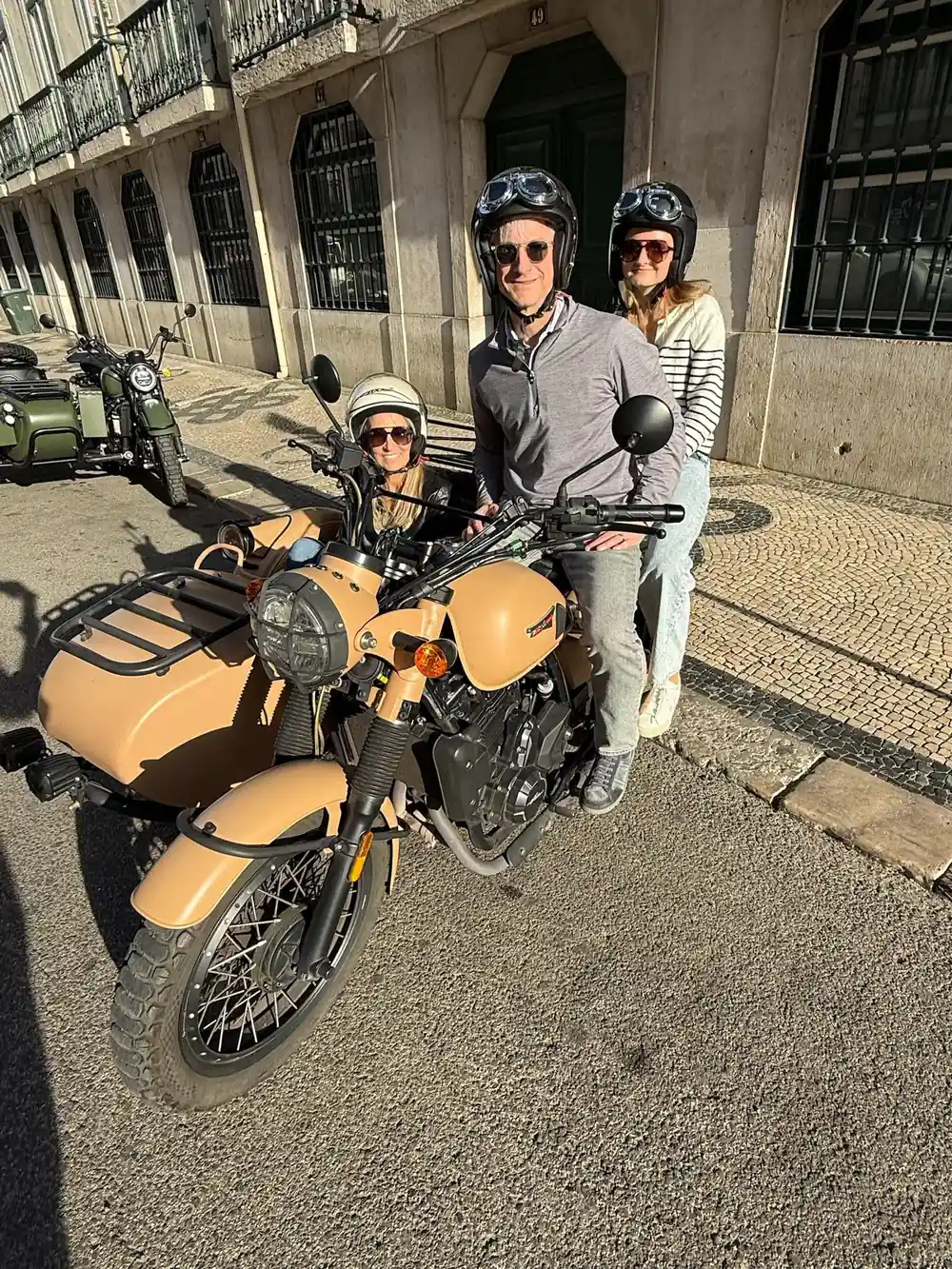 Three people beside a tan sidecar on a mosaic paved square