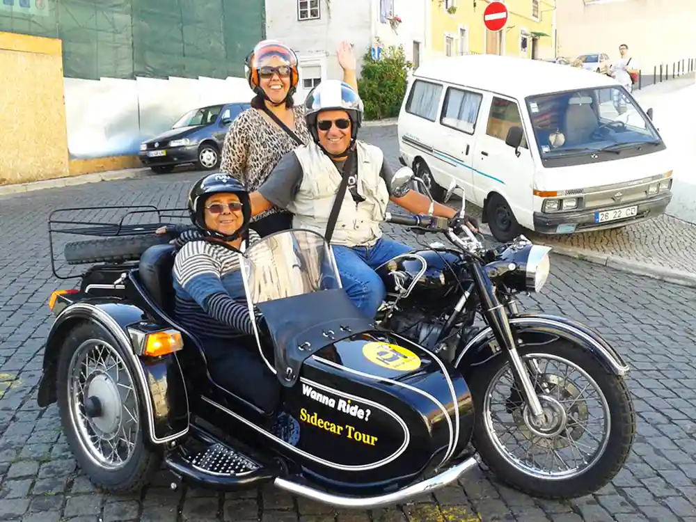 Three riders with a black sidecar on cobbles, operator lettering on the chair