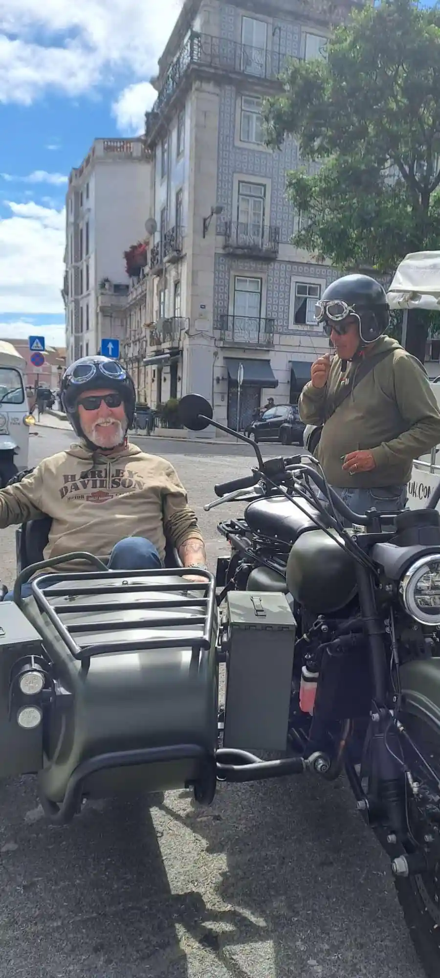 Two men with a sidecar on a city street, one seated in the chair