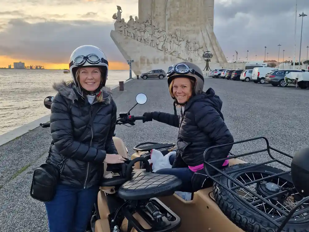 Two riders on a sidecar at the Monument to the Discoveries in low sun
