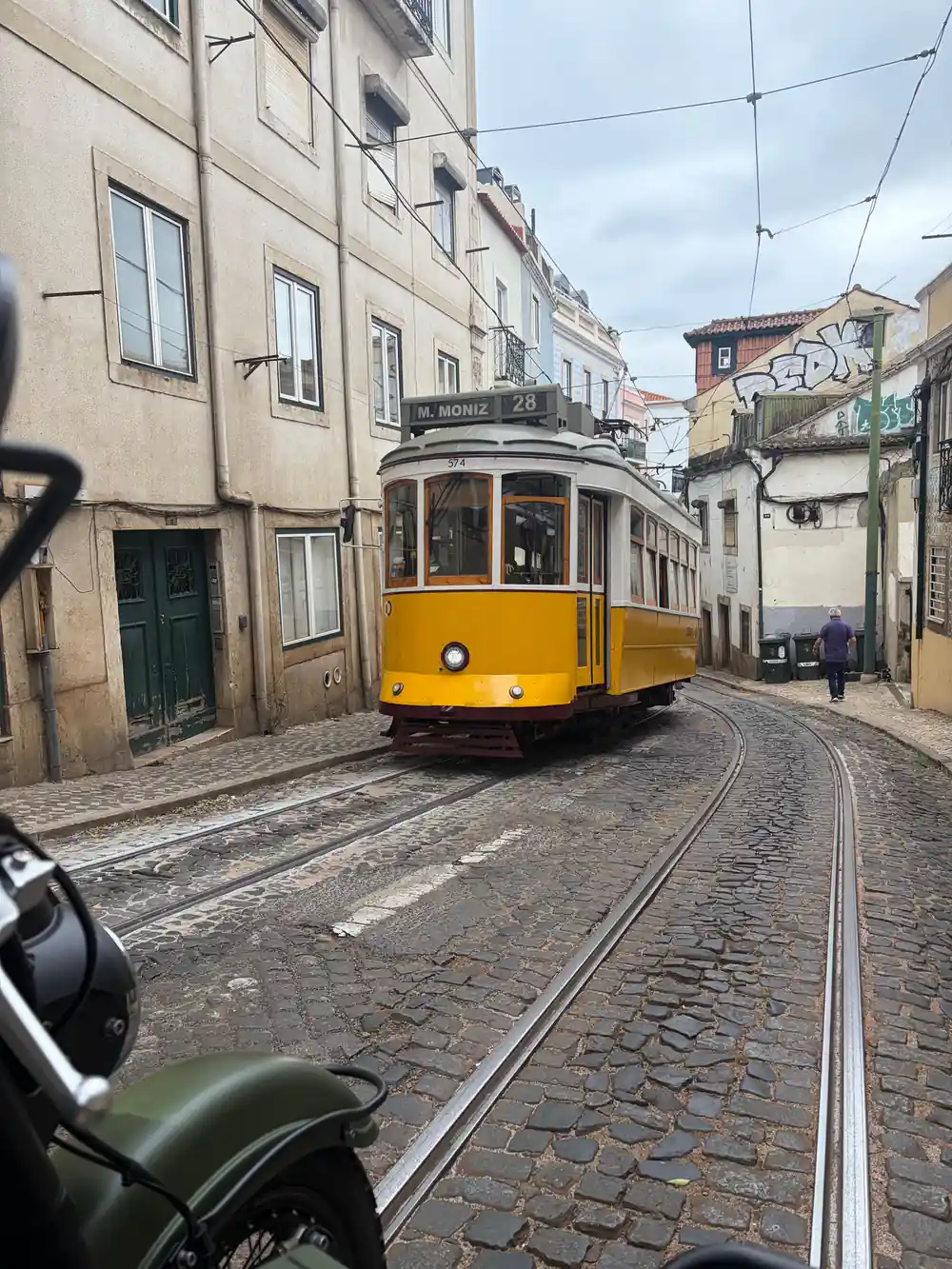 A yellow tram on cobbled rails in a narrow street, seen past a sidecar mirror